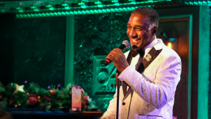 Norm Lewis at the Microphone at 54 Below in a white tux jacket with a twinkle in his eye